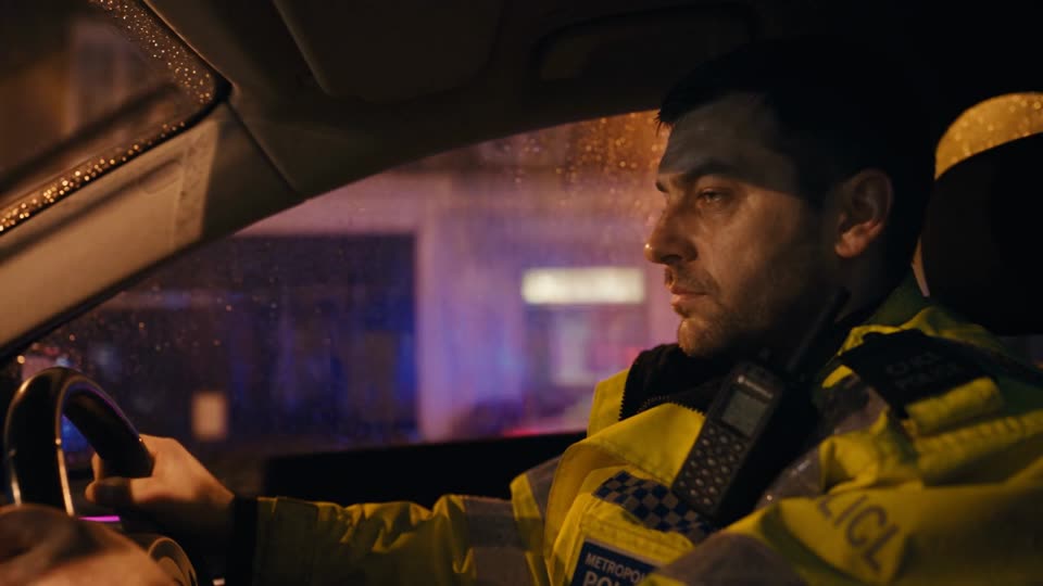 PC Arthur at the wheel of a patrol car at night, rain on the windows